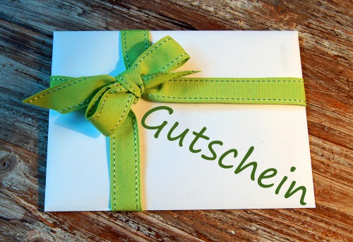 Geschenkgutschein mit grüner Schleife auf Holz